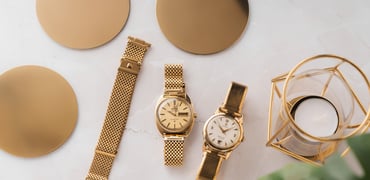 gold-plated Forstner Komfit Mesh and Military Type bracelets on Omega Constellation and Seamaster, flat-lay with gold coasters and candle