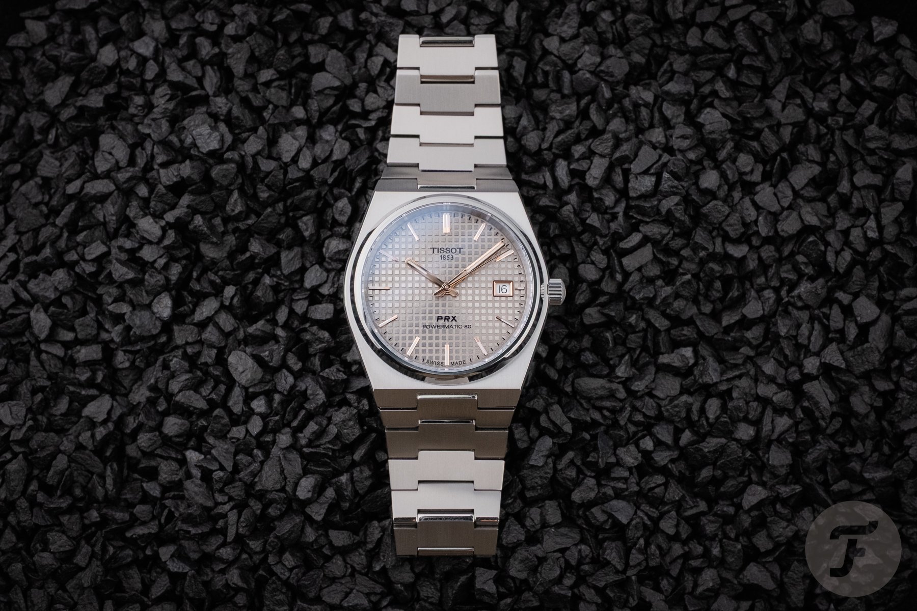 Tissot PRX Titanium 38mm flat-lay on black pebbles