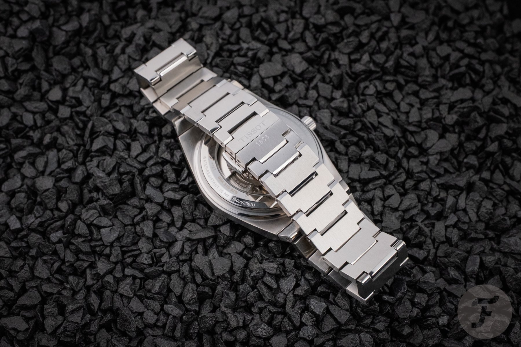 Tissot PRX Titanium 38mm face down on black pebbles, clasp closed