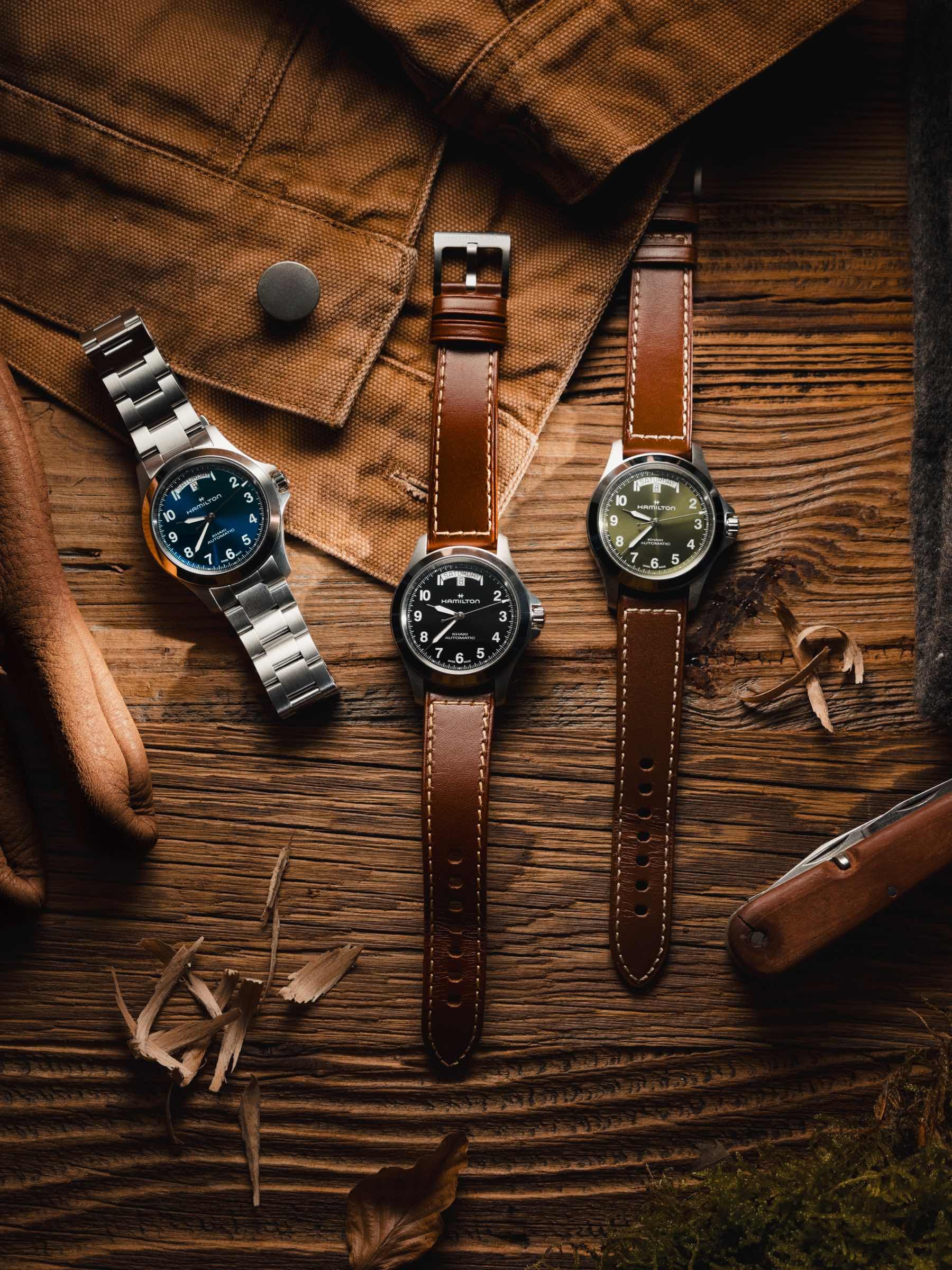 three Hamilton Khaki Field King Day-Date Automatic watches on a wooden surface, top-down photo