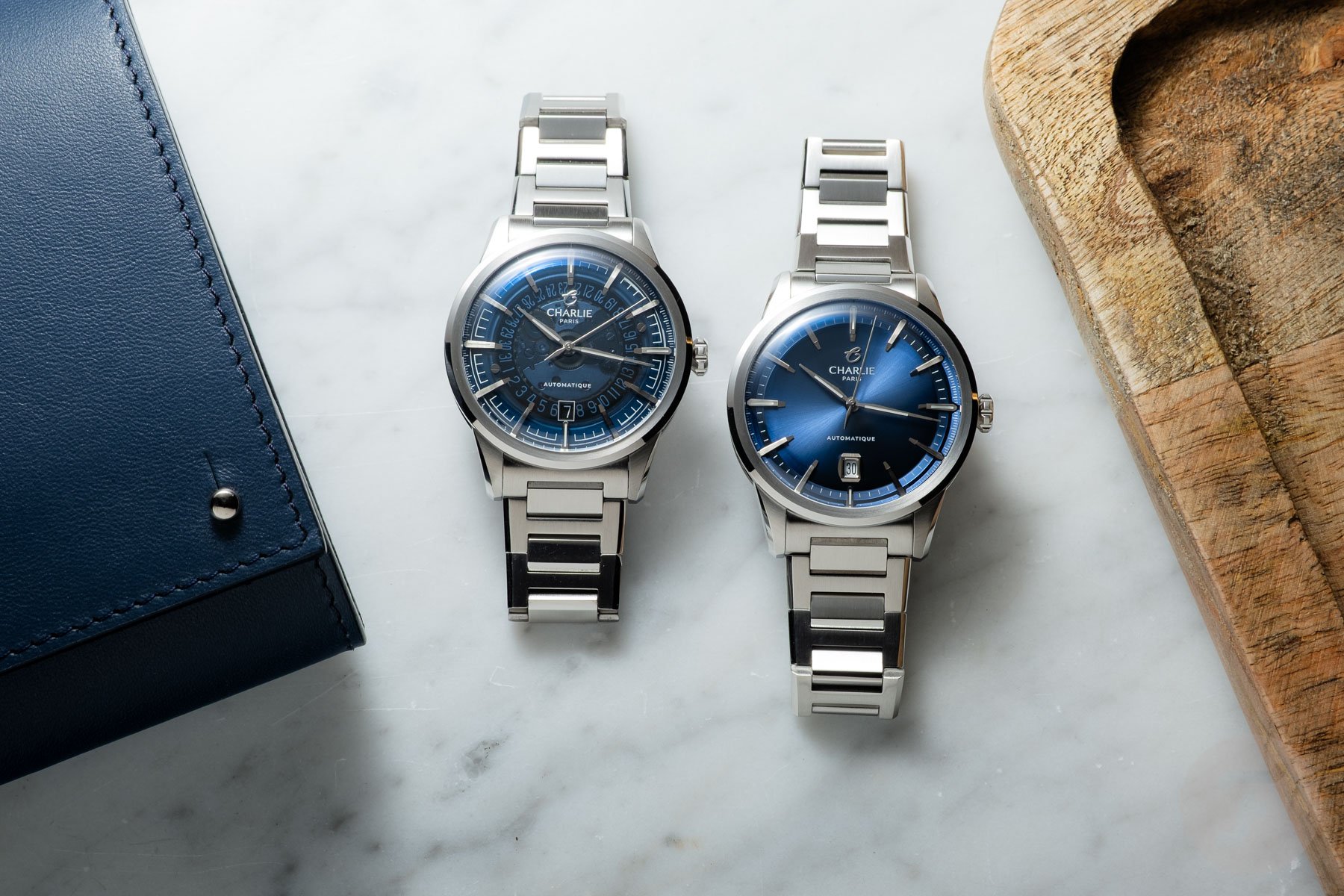 Charlie Paris Alliance blue sunburst and blue sapphire dial side by side on a marble surface