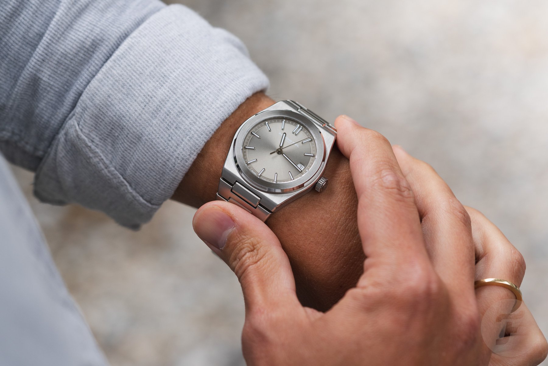 gray-dial Raymond Weil A.R.T. on wrist, fingers on bracelet