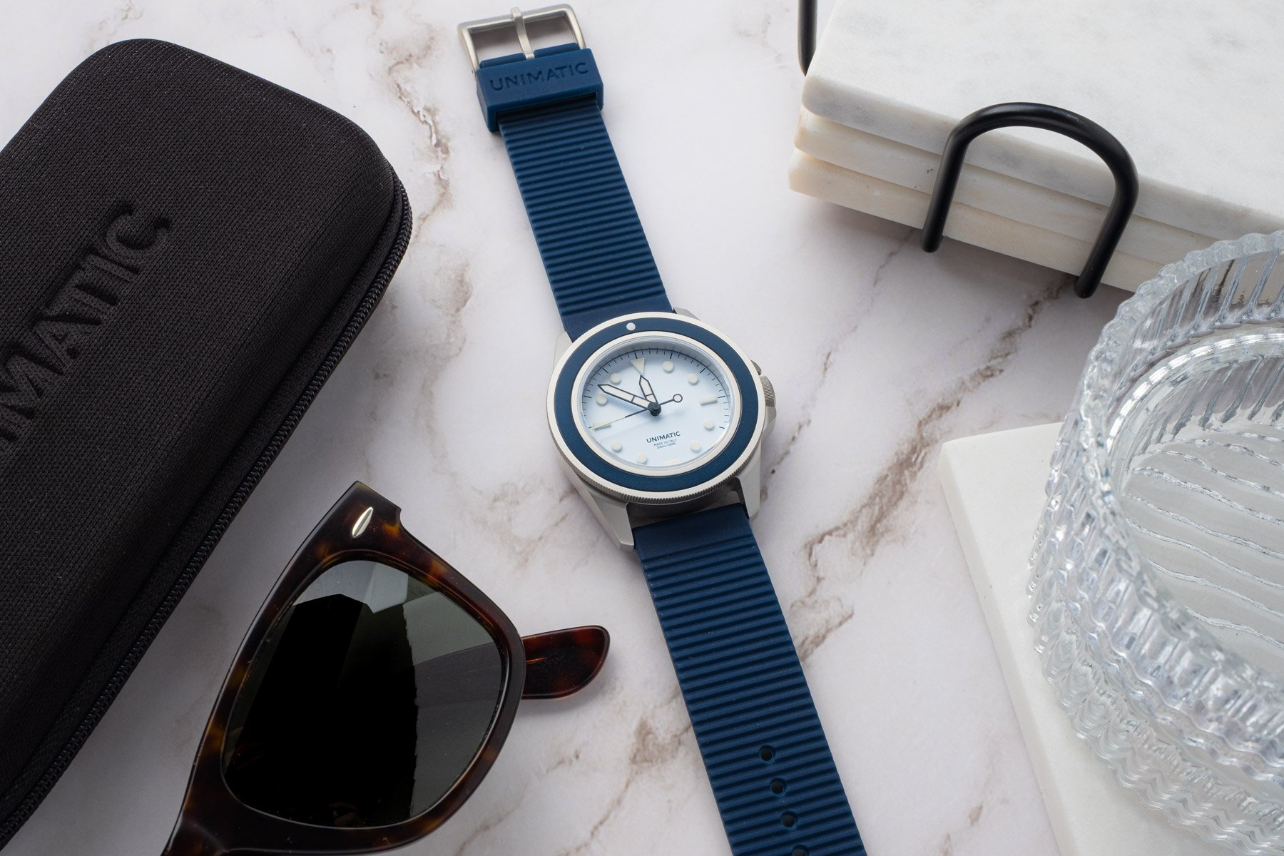 Unimatic Modello Uno UT1-IPP flat-lay with travel case, sunglasses, glass bowl, and marble tiles