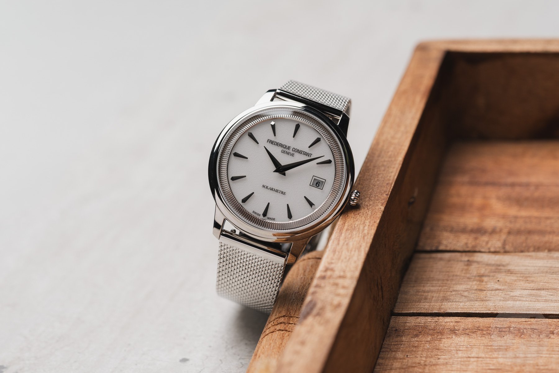 white-dial Frederique Constant Moneta Solarmetre on mesh leaning on a wooden tray