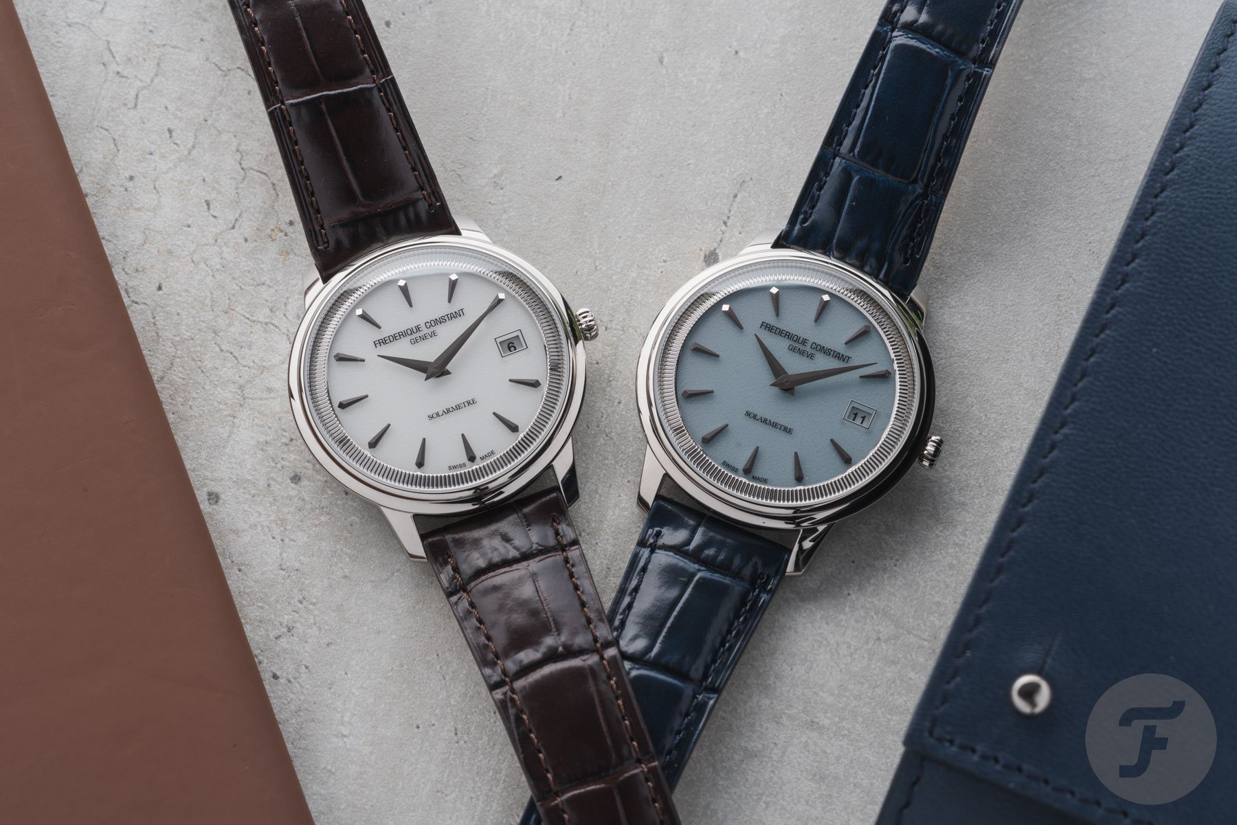 white- and blue-dial Frederique Constant Moneta Solarmetre models next to each other, flat-lay