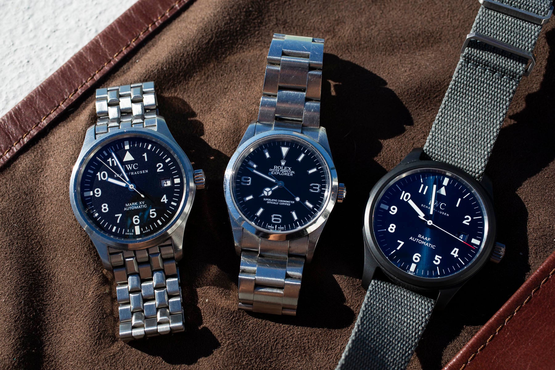 Rolex Explorer ref. 114270, IWC Mark XV, and IWC RAAF Pilot's Watch lined up, flat-lay