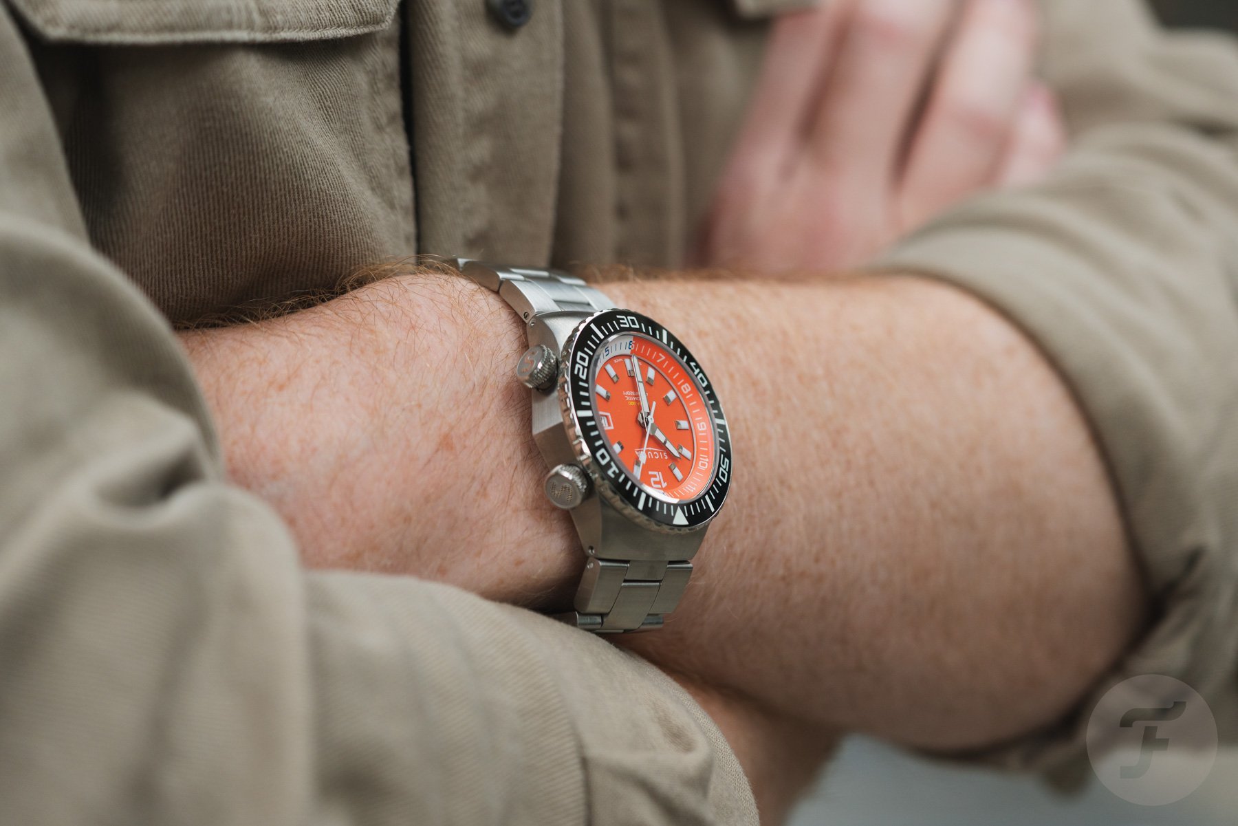 orange-dial Sicura Hexa 400 on wrist, arms crossed