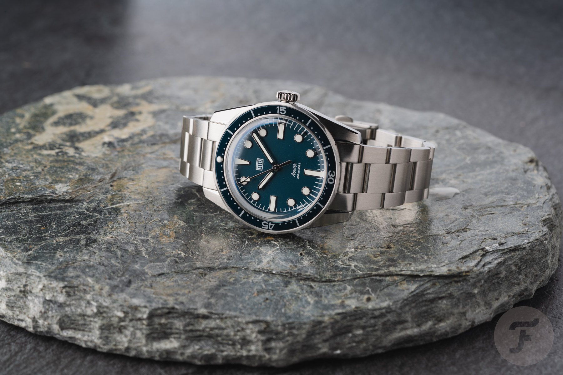blue-dial HTD Aquatìc Bicchierini on its side, crown up, on top of stone slab