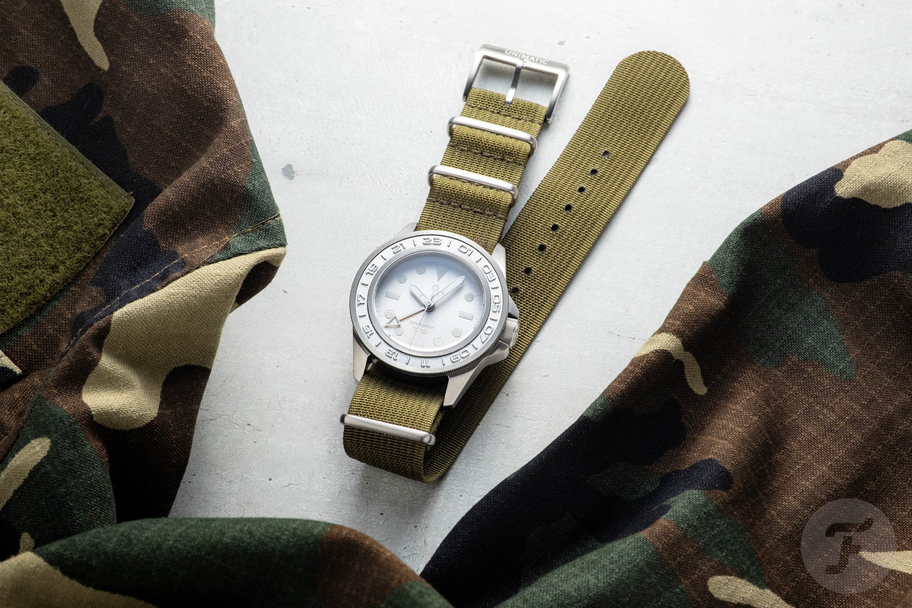 Unimatic Modello Uno GMT Impronte U1-GMT-AEG flat-lay with camo jacket