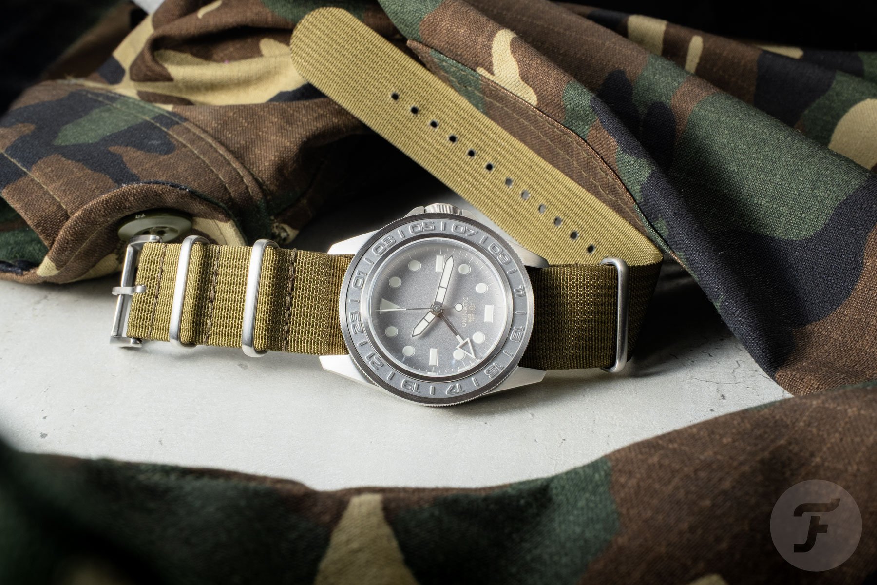 Unimatic Modello Uno GMT Impronte U1-GMT-AEG on its side, crown up, with camo jacket