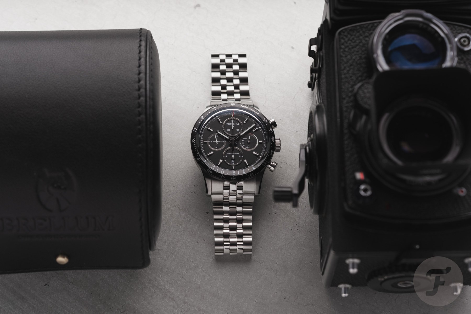 black-dial Brellum Pandial 43 Power Reserve LE Chronometer Pandial 43 Power Reserve LE Chronometer DB.CH.955 flat-lay between camera and watch pouch
